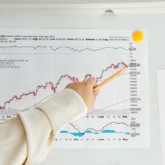 Close-up of a woman's hand pointing to data trends on a stock market chart using a pencil.