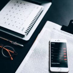 High angle shot of a desk setup with smartphone displaying stock market analytics, clipboard, pen, and glasses.