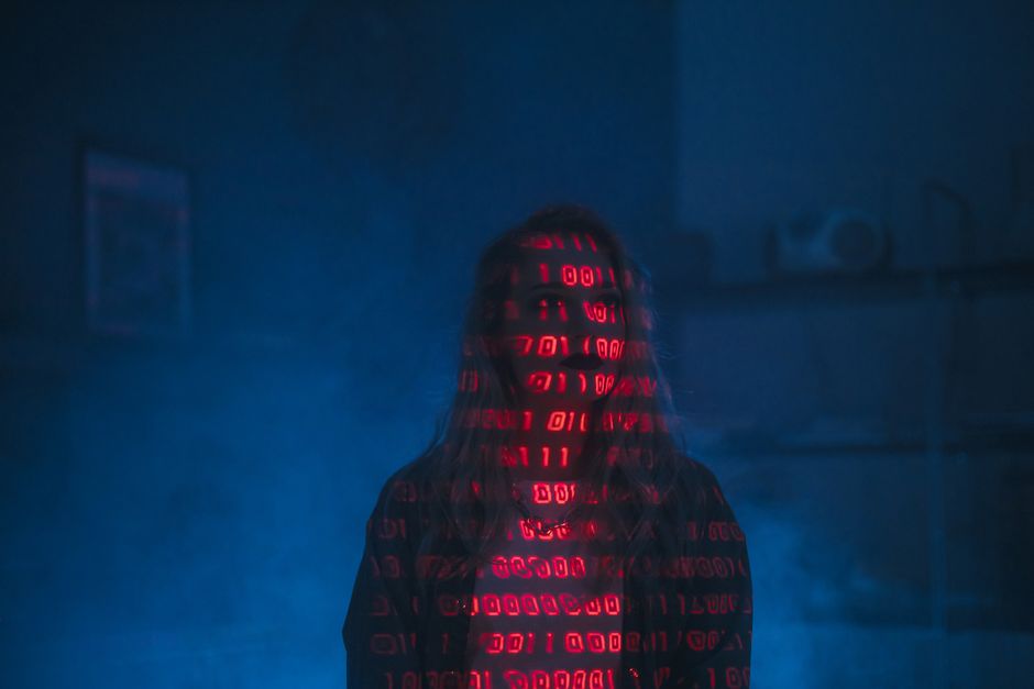 A mysterious silhouette with red binary code projected over the face, set against a dark, moody background.