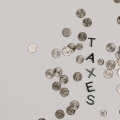 Scattered coins forming the word 'TAXES' on a white surface, symbolizing financial concepts.