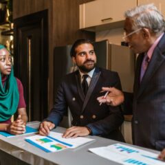 Three business professionals engage in a discussion, showcasing diversity and teamwork in a modern office setting.