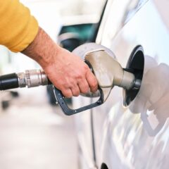 Close-up of a person refueling a car with a gas nozzle at a station.
