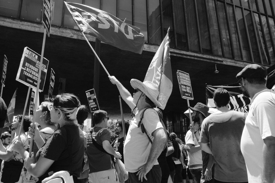 Crowd holds flags and signs during protest in urban setting.