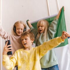 Three children happily take a selfie with a flag in the background, celebrating friendship and fun.