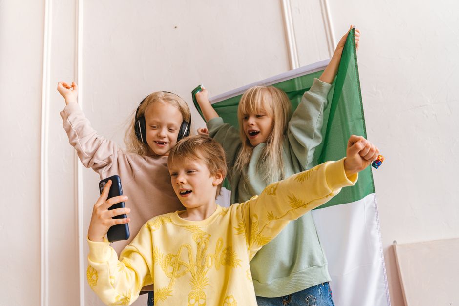 Three children happily take a selfie with a flag in the background, celebrating friendship and fun.