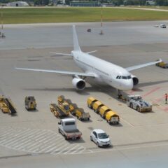 High angle view of a commercial airplane on airport tarmac with ground support vehicles.