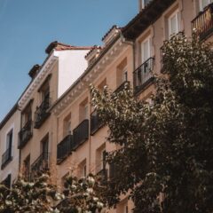 Elegant residential building with balconies and lush trees in Madrid, Spain.