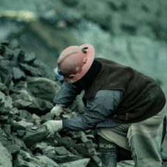 A coal miner in a hard hat working amidst rocky terrain, emphasizing labor and resilience.