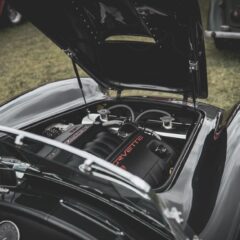 A classic sports car with an open hood revealing a Corvette engine in a vintage car show.