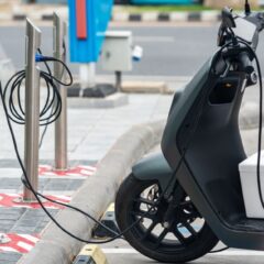 Electric scooter plugged into a charging station in a city environment, showcasing eco-friendly urban transportation.