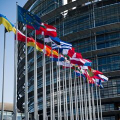 Flags of European Union countries outside a modern building facade.