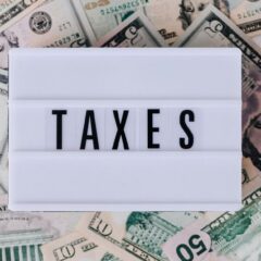 Top view of white vintage light box with TAXES inscription placed on stack of USA dollar bills on white surface