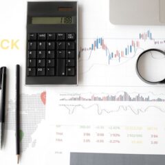 Flat lay of stock market analysis tools including calculator, graphs, and magnifying glass.