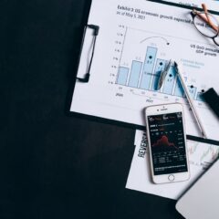 Top view of financial reports, smartphone showing stock market data, and a laptop on desk.