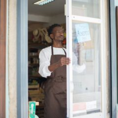 A man in an apron opens a grocery store door in Portugal, ready for business.