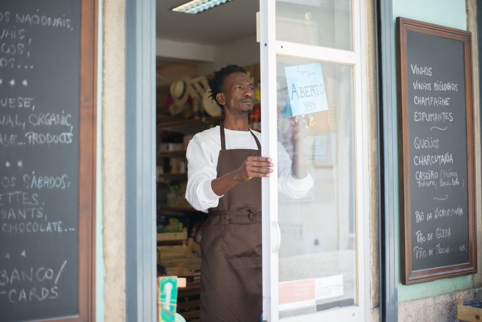 A man in an apron opens a grocery store door in Portugal, ready for business.