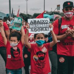 Protesters rallying against Bolsonaro in Rio de Janeiro, showing signs and wearing masks amidst the crowd.