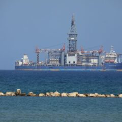 An offshore drilling rig floats on a calm sea with a clear blue sky in the background.