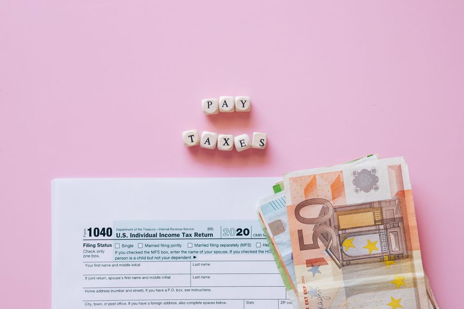Top view of tax form, euro banknotes, and 'Pay Taxes' letter blocks on pink background.